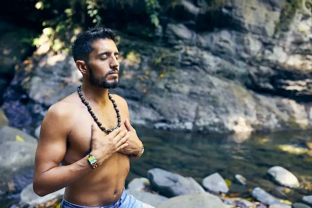 alt="a man meditating near a river"